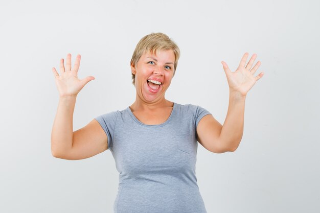 Mulher loira levanta as mãos e regozijando-se na camiseta azul claro e parecendo feliz. vista frontal.