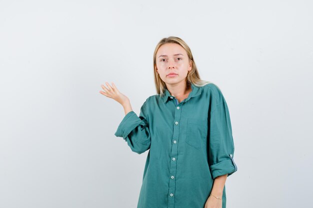 Mulher loira levantando espalhar palm na camisa verde e olhando pensativa.