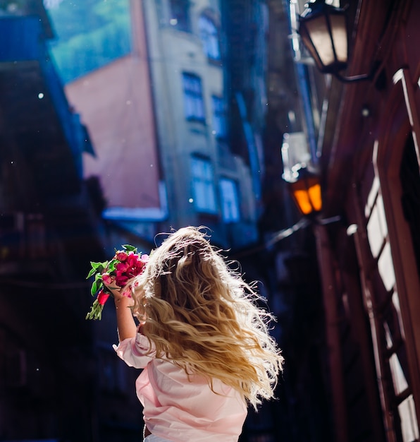 Foto grátis mulher loira mantém um buquê de peônias cor-de-rosa girando na rua