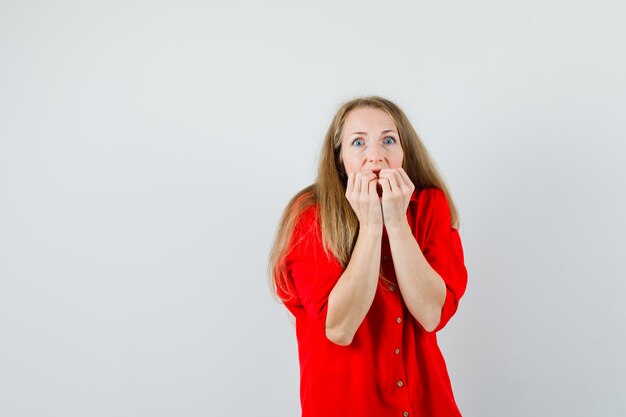 Mulher loira mordendo os punhos emocionalmente em uma camisa vermelha e parecendo assustada,