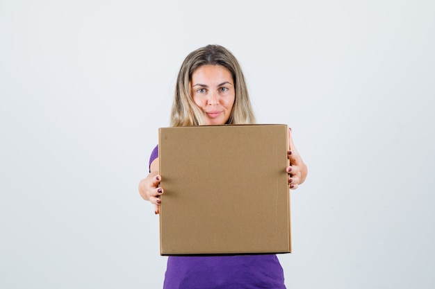 Mulher loira mostrando a caixa de papelão na vista frontal da camiseta violeta.