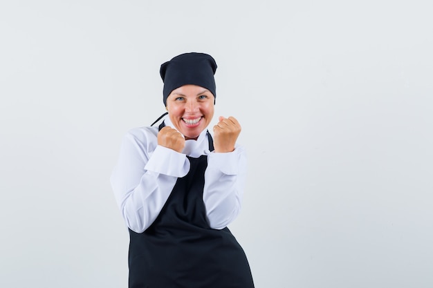 Mulher loira mostrando gesto de sucesso em uniforme de cozinheiro preto e parecendo feliz. vista frontal.
