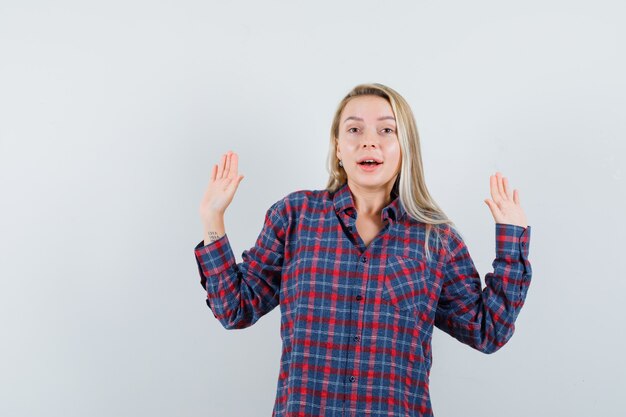 Mulher loira mostrando pose de rendição em camisa xadrez e atraente. vista frontal.