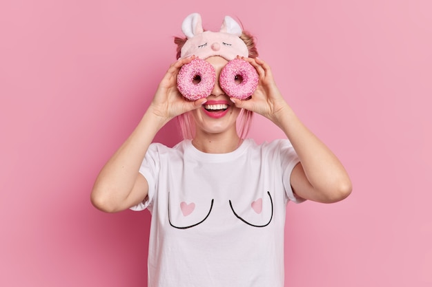 Foto grátis mulher loira positiva segurando rosquinhas deliciosas sobre os olhos, sorrindo, mostrando dentes perfeitos