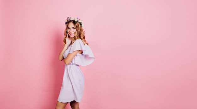 Mulher loira refinada com vestido de verão em pé perto da parede rosa com um sorriso