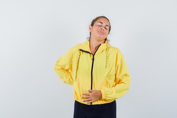 Foto grátis mulher loira segurando a mão na barriga e tendo dor de barriga com uma jaqueta amarela e calça preta e parecendo exausta