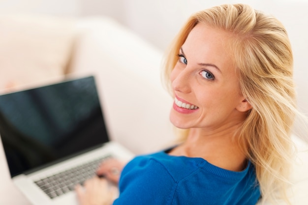 Mulher loira sentada em casa com laptop