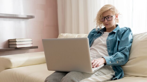 Mulher loira sentada no sofá e trabalhando no laptop