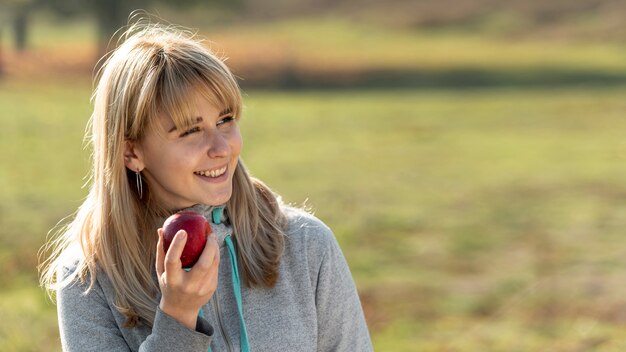 Mulher loira sorridente, comendo uma maçã deliciosa