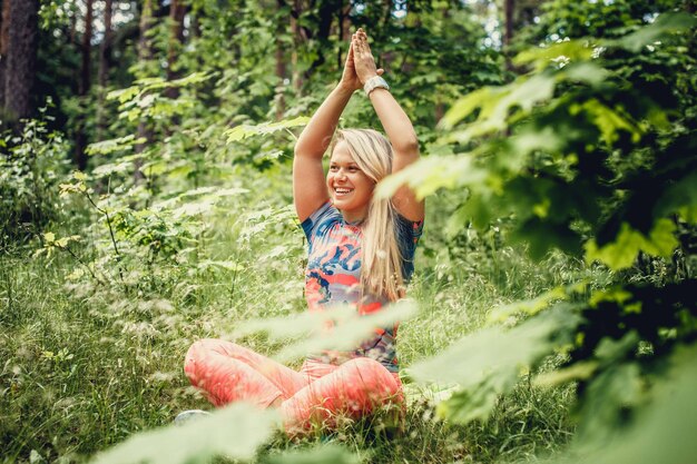 Mulher loira sorridente fazendo ioga na floresta.