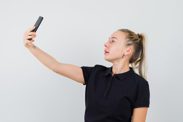 Mulher loira tirando selfie com camiseta preta