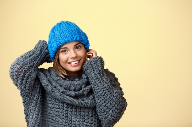 Mulher loura bonita nova no chapéu e na camisola knited que sorriem no amarelo.