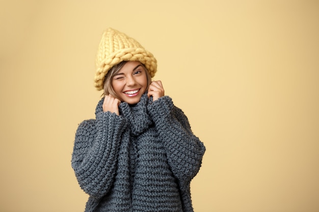 Foto grátis mulher loura bonita nova no chapéu e na camisola knited que sorriem piscando no amarelo.