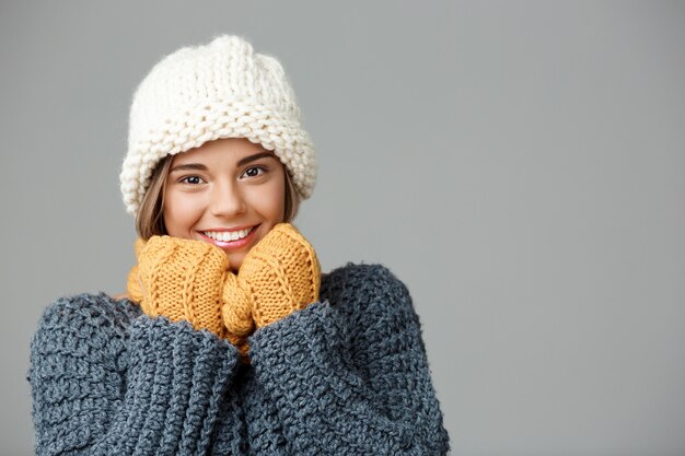 Mulher loura bonita nova no lenço da camisola do chapéu knited e nas luvas que sorriem no cinza.