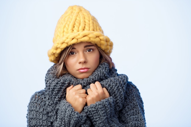 Mulher loura bonita triste nova no chapéu e na camisola knited no azul.