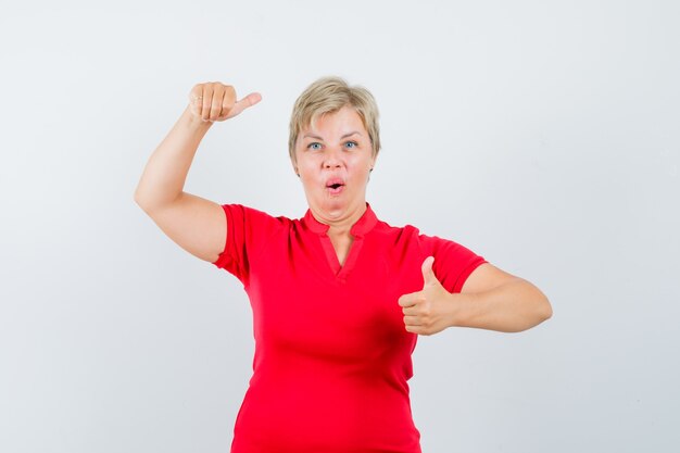 Mulher madura aparecendo o polegar, fingindo segurar algo em uma camiseta vermelha