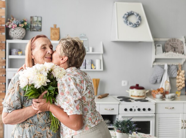 Mulher madura, beijando, dela, mãe, segurando, flor branca, buquê, casa