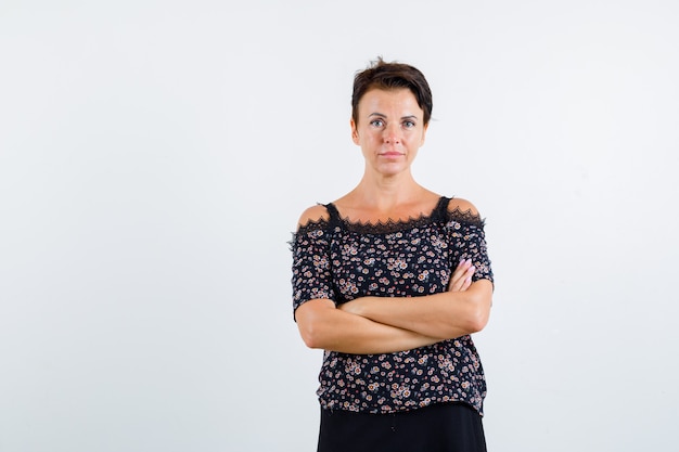 Foto grátis mulher madura com blusa floral e saia preta em pé com os braços cruzados e olhando confiante, vista frontal.