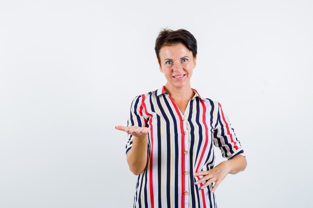 Mulher madura com camisa listrada, estendendo a mão e olhando alegre, vista frontal.