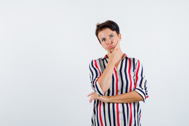 Foto grátis mulher madura com camisa listrada, segurando o queixo enquanto pensa e parece confusa, vista frontal.