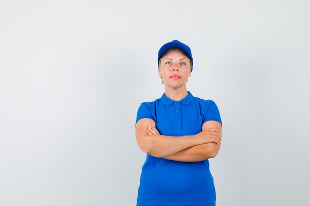 Mulher madura em pé com os braços cruzados em uma camiseta azul e olhando séria