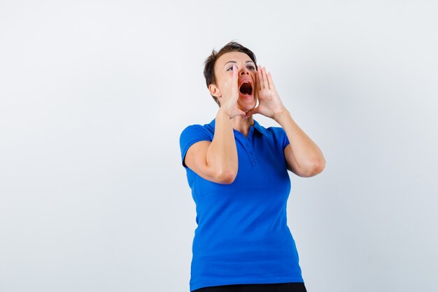 Mulher madura em t-shirt azul gritando ou anunciando algo e olhando animado, vista frontal.