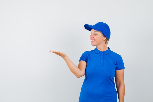 Mulher madura em t-shirt azul, olhando para a palma da mão espalhada e parecendo esperançosa.