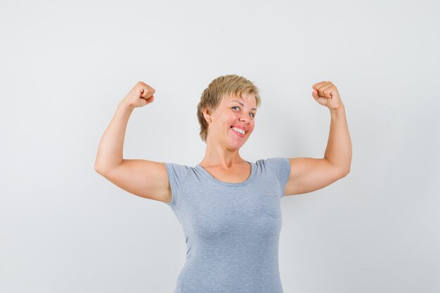 Mulher madura em uma camiseta cinza mostrando os músculos dos braços e parecendo forte