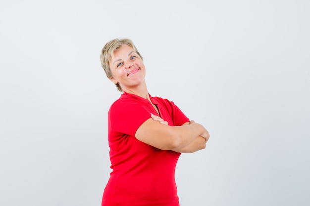 Mulher madura em uma camiseta vermelha em pé com os braços cruzados e parecendo orgulhosa