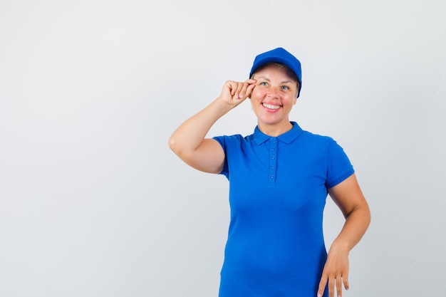 Mulher madura fingindo fazer maquiagem em camiseta azul e parecendo alegre.