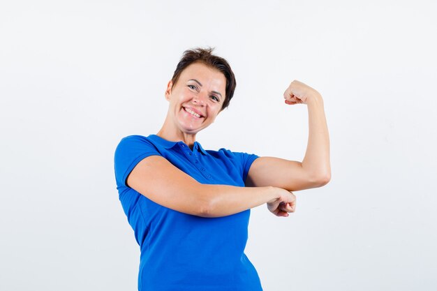 Mulher madura mostrando os músculos do braço em t-shirt azul e parece feliz. vista frontal.