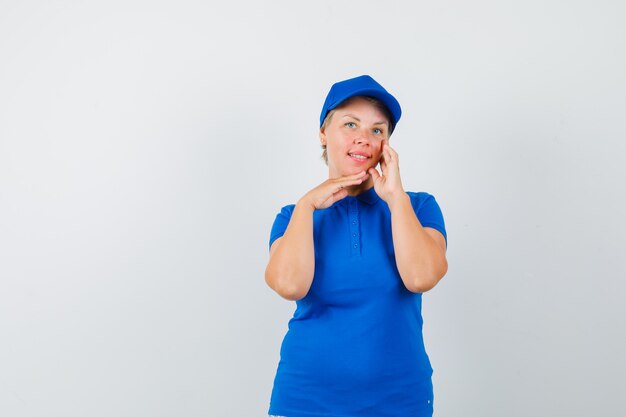 Mulher madura posando ao tocar a pele do rosto em t-shirt azul.