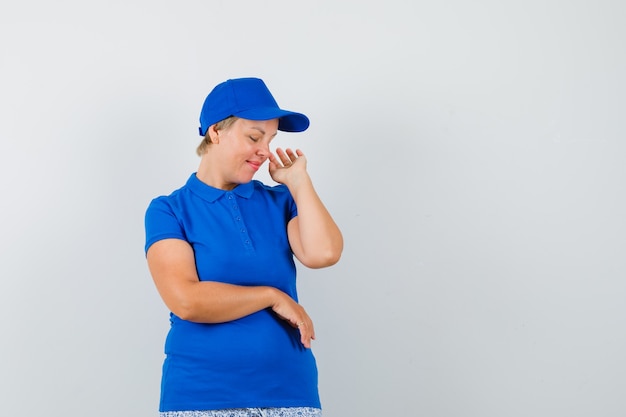 Mulher madura posando enquanto olha para baixo em t-shirt azul e parece fofo.