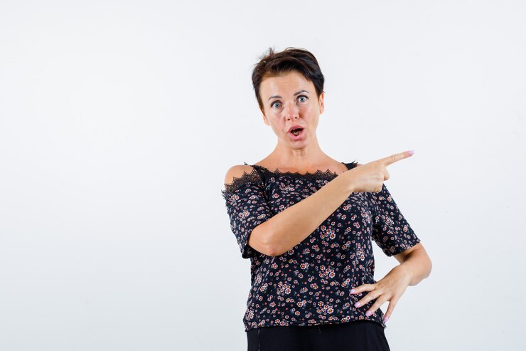 Foto grátis mulher madura segurando a mão na cintura, apontando para a direita com o dedo indicador