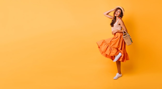 Mulher magnífica com saia longa e brilhante dançando no estúdio. Modelo feminino inspirado despreocupado posando com prazer em amarelo.