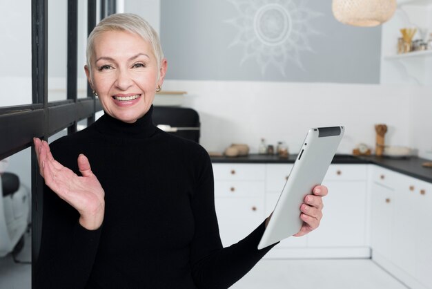 Mulher mais velha feliz na cozinha segurando o tablet