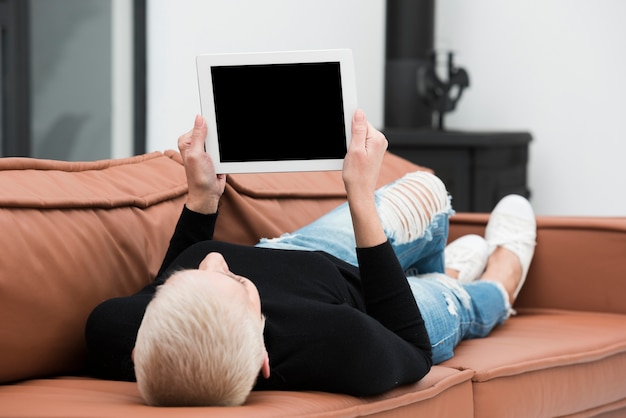 Foto grátis mulher mais velha, relaxando no sofá e segurando o tablet