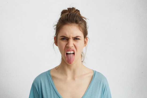 Foto grátis mulher mal-humorada com nó de cabelo, mostrando a língua expressando emoções negativas. mulher furiosa mostrando nojo enquanto briga