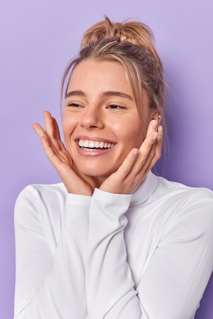 Mulher mantém as mãos nos sorrisos de bochechas amplamente com dentes brancos vestidos casualmente isolados em roxo. conceito de emoções e expressões faciais de pessoas felizes