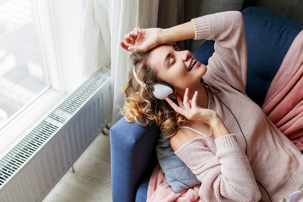 Mulher maravilhosa com cabelos curtos encaracolados ouve música favorita e deitada com os olhos fechados com prazer. Vestindo um lindo loungewear rosa.