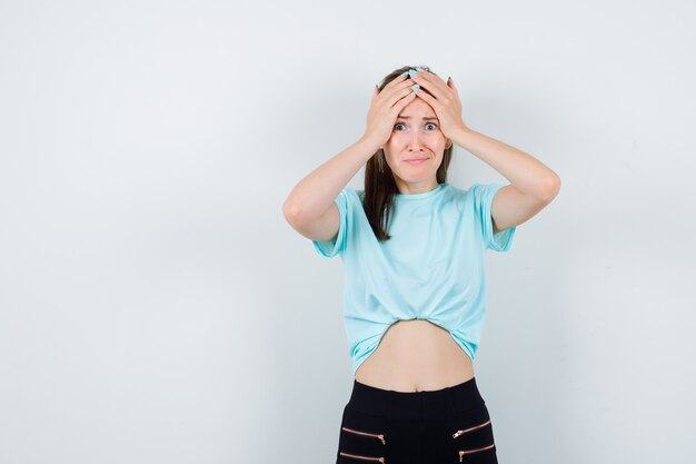 Mulher maravilhosa na blusa, calça, mantendo as mãos na cabeça e parecendo deprimida, vista frontal.