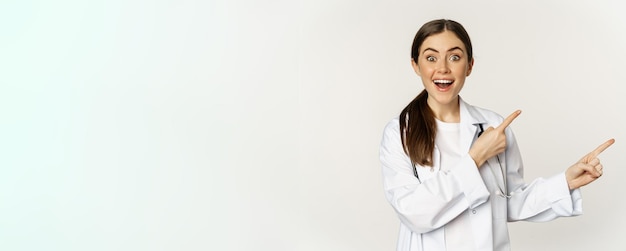 Mulher médica em uniforme médico apontando dedos para a direita mostrando anúncio de banner sorrindo