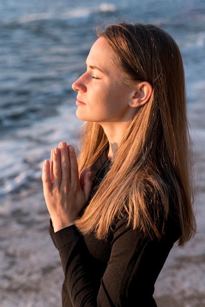 Foto grátis mulher meditando de lado na praia