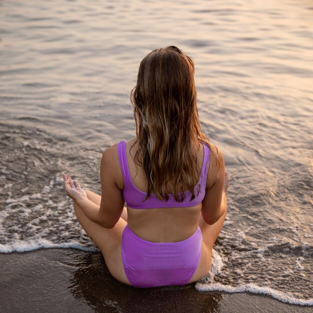 Mulher meditando na praia em maiô