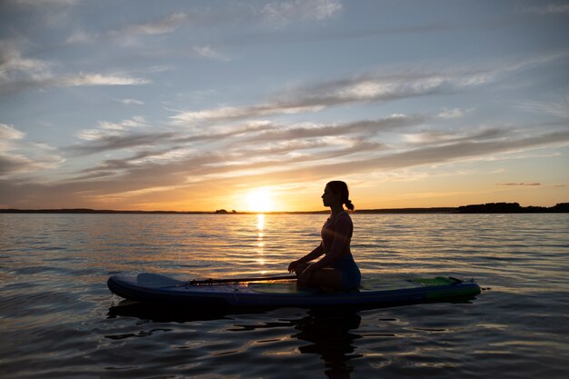 Mulher meditando na vista lateral do paddleboard