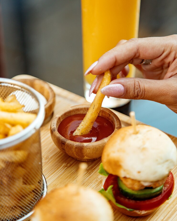 Foto grátis mulher mergulhando batatas fritas em ketchup