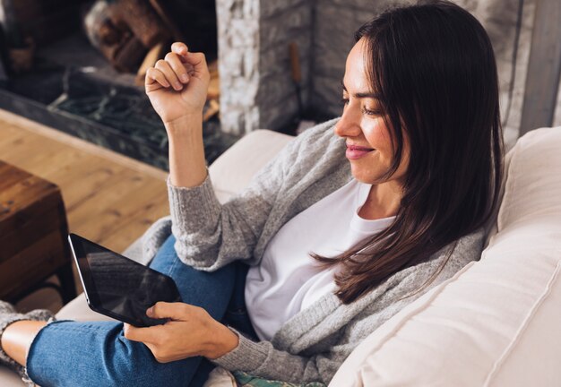 Mulher moderna sentada no sofá usando um tablet