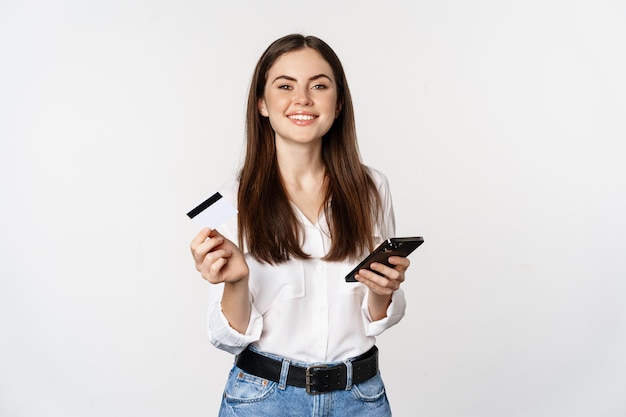 Mulher moderna sorridente usando cartão de crédito e telefone celular pagando comprando compras on-line em sm...