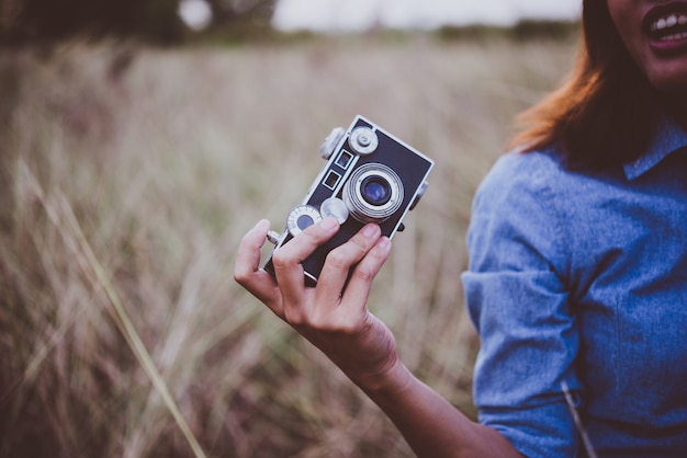 Mulher moderno novo que faz fotos com câmera de filme do vintage no campo do verão. Mulheres estilo de vida conceito.