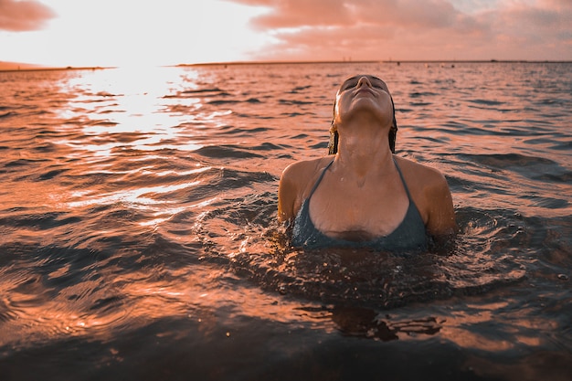 Mulher morena cacheada posando no oceano sob o céu nublado do pôr do sol